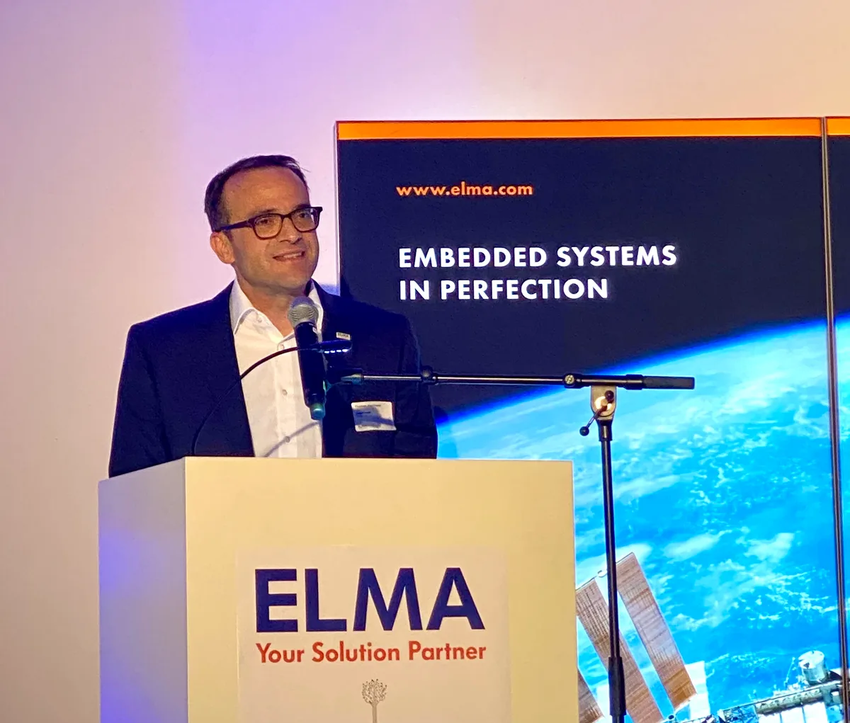 Ein Mann steht hinter einem Rednerpult, das mit «Elma» beschriftet ist.